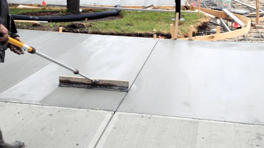 Fresh concrete being broom-finished on a newly poured driveway slab