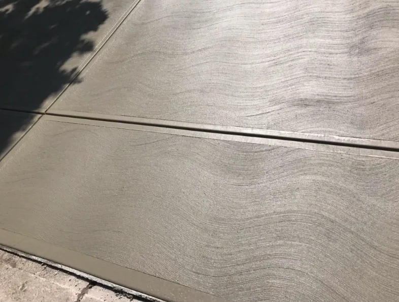Close view of a broom-finished concrete driveway surface beside a cut control joint