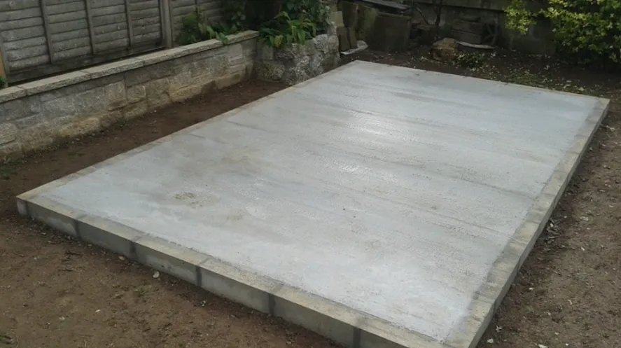 Freshly poured concrete pad sized for a shed in a residential back yard